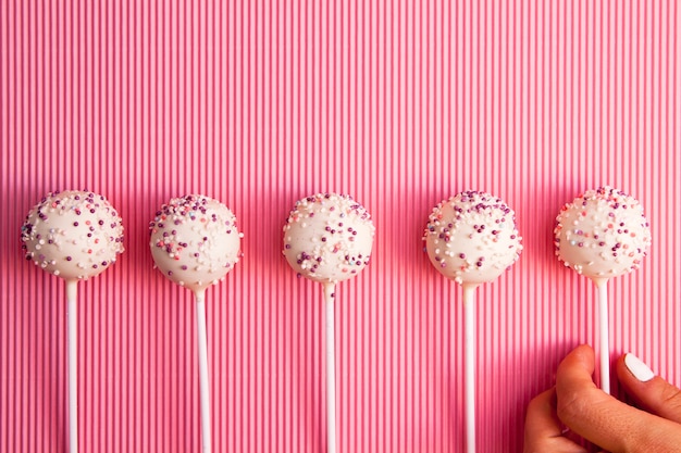 Cake aparece en un palo en una fila en una superficie rosa con la mano. Dulces sabrosos y hermosos