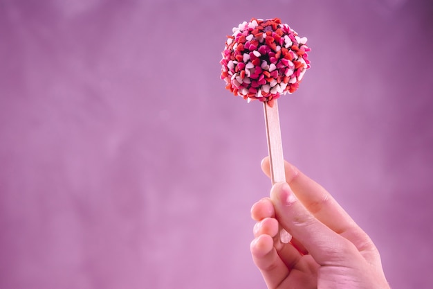 Cake pop en un palo con una pizca de corazones en la mano