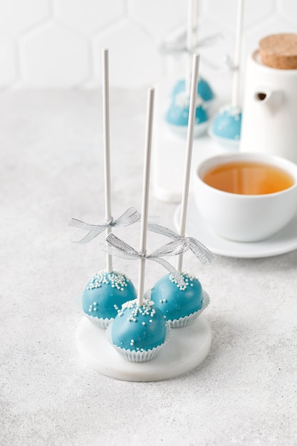 Cake Pops auf Stöcken Satz von blauen Cake Pops mit Tasse Tee auf grauem Hintergrund Süßes hausgemachtes Dessert