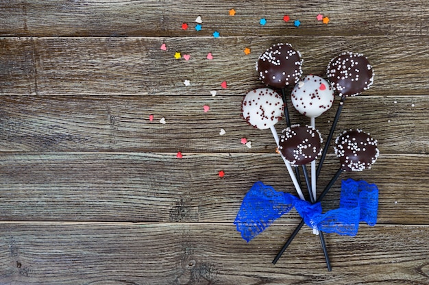 Cake Pops. Süße Süßigkeiten in weißer und schwarzer Schokoladenglasur, auf einem Stock auf einem hölzernen Hintergrund.