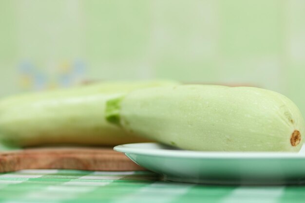 Un calabacín entero en un plato blanco y una tabla de madera sobre un mantel verde Verduras saludables Primer plano