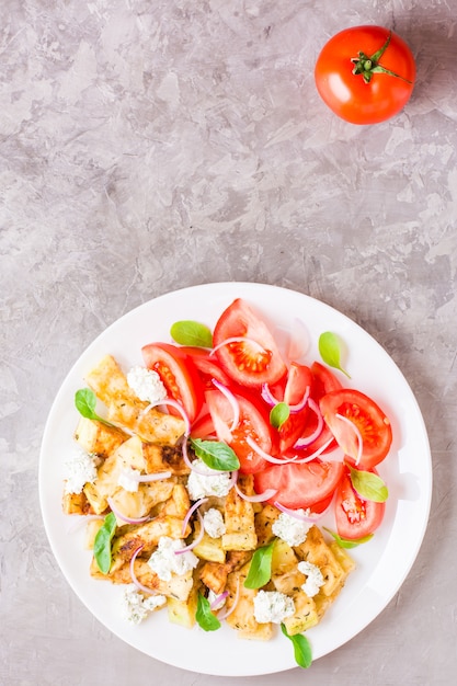 Calabacín frito con queso feta, tomates, hierbas y cebollas en un plato sobre una mesa