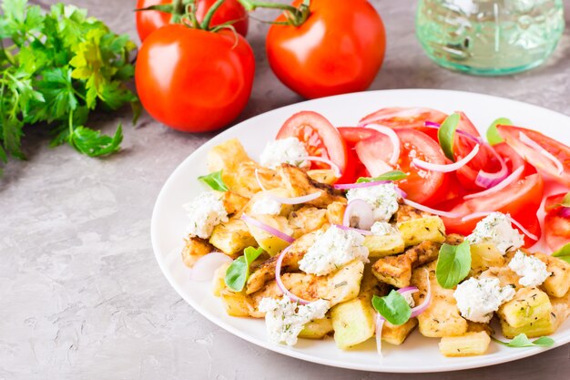 Calabacín frito con queso feta, tomates, hierbas y cebollas en un plato sobre una mesa