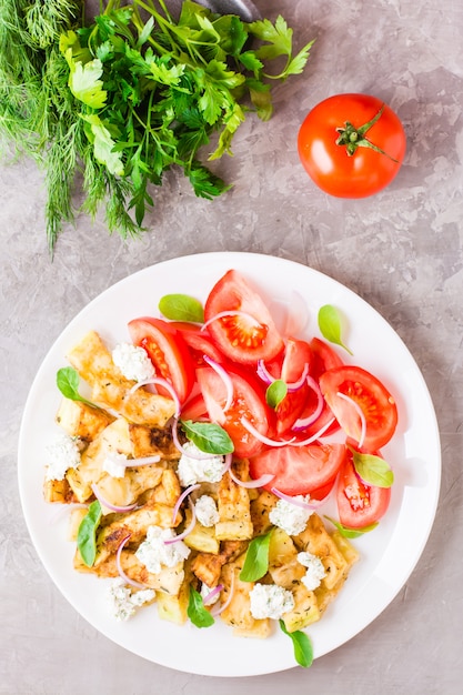 Calabacín frito con queso feta, tomates, hierbas y cebollas en un plato