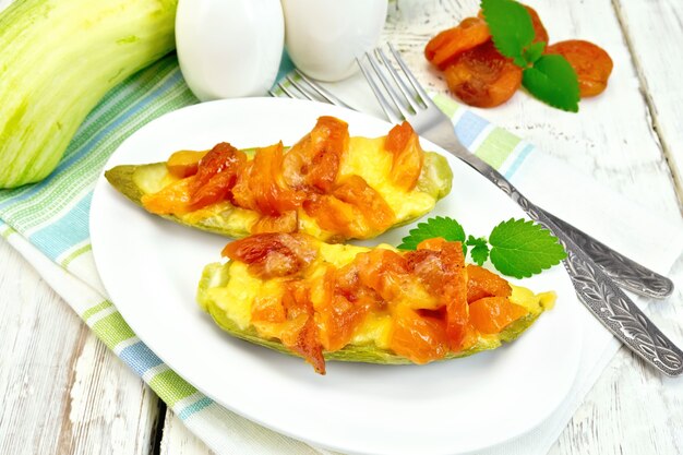 Calabacín joven horneado en una salsa aromatizada con albaricoque seco, crema y queso en un recipiente sobre una toalla sobre el fondo de tablas de madera