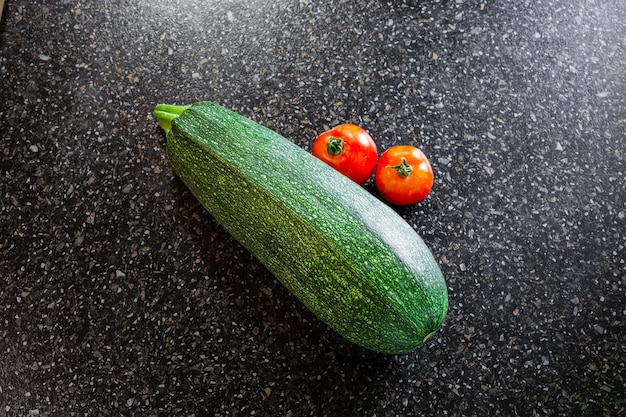 Calabacín rayado verde y tomates rojos sobre un fondo negro Cosecha de verduras de verano