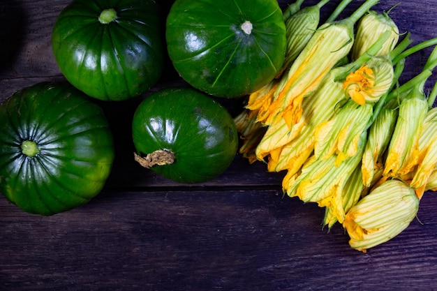 Foto calabacín de tronco verde para cocinar y flores sobre madera rústica.