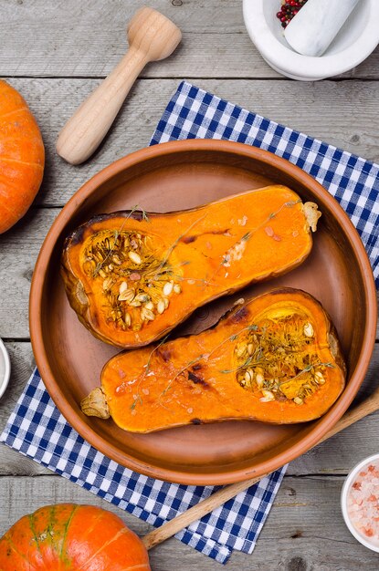 Calabaza al horno con tomillo en un plato de arcilla en una servilleta azul, en una mesa de madera