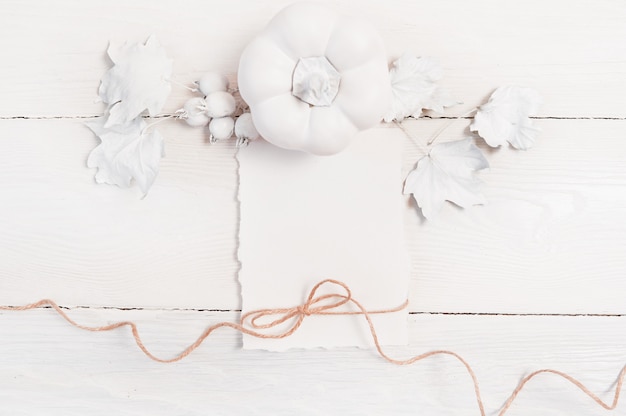 Calabaza blanca, bayas y hojas y hoja blanca de papel y cuerda de lino