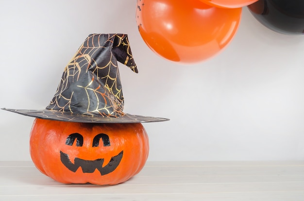 Calabaza con cara pintada en sombrero de bruja cerca de globos naranjas y negros