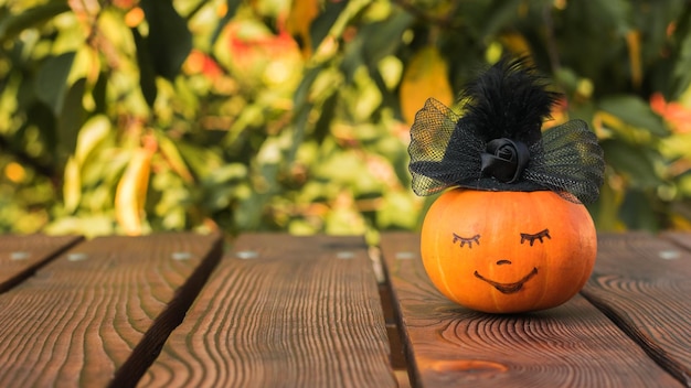 Calabaza con una cara sonriente en un sombrero negro sobre una mesa de madera