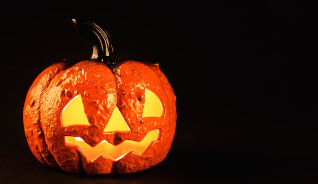 Calabaza de cerámica con una cara espeluznante con una vela que brilla intensamente en el interior como una linterna para la noche de halloween aislada sobre fondo negro con espacio de copia