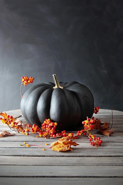 Calabaza de color negro con bayas y hojas en la mesa