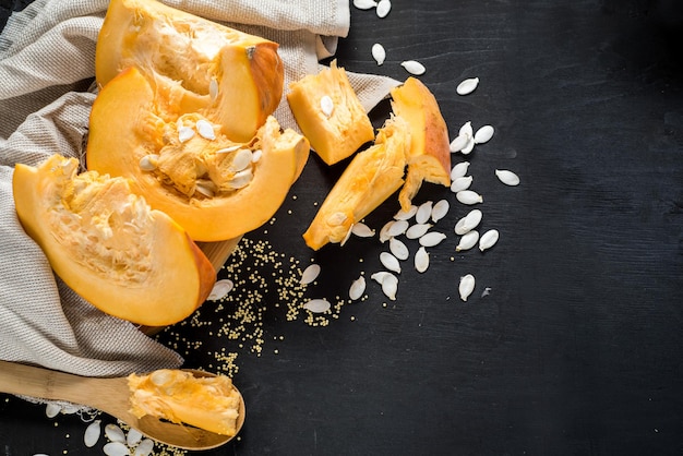 Calabaza cruda grande cortada en trozos sobre fondo de madera negra. copia espacio