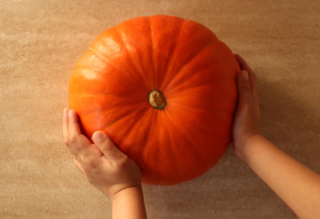 Calabaza fresca redonda naranja en manos de los niños sobre un fondo beige