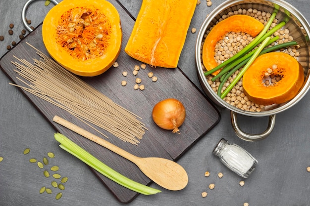 Calabaza y garbanzos en una cacerola Fideos media cuchara de madera de calabaza y tallos de apio en la tabla de cortar