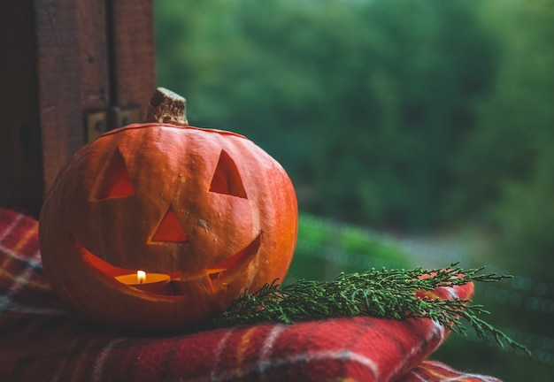 Calabaza de Halloween en un acogedor alféizar de la ventana con una tela escocesa roja. Calabaza entera y bengala al aire libre. ¡Feliz Halloween! El otoño es acogedor.