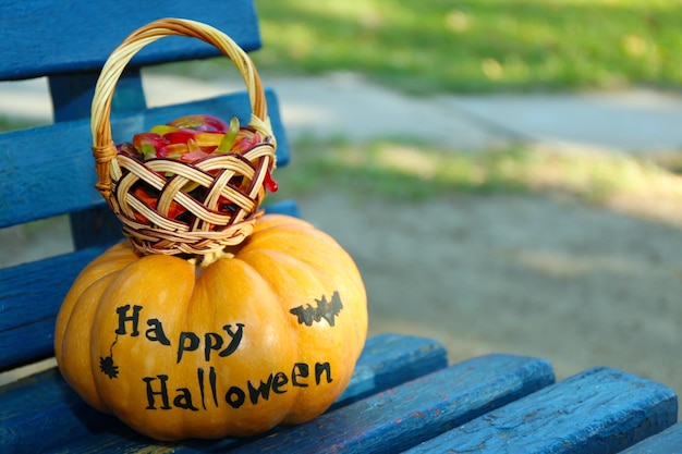 Calabaza de Halloween y canasta con dulces en el fondo de un banco colorido al aire libre