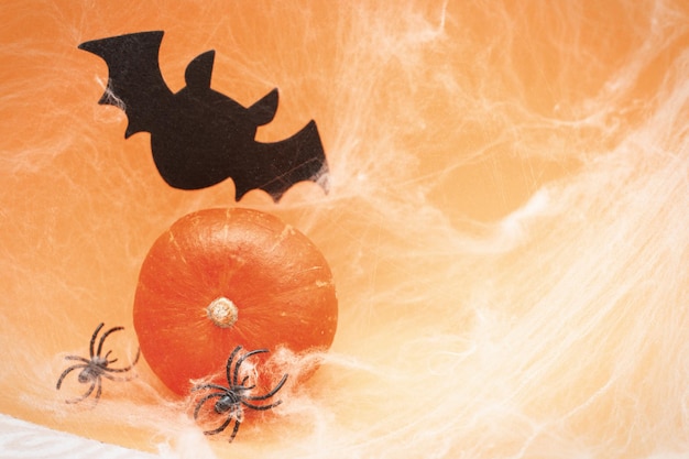 Foto calabaza de halloween con murciélago de tela de araña y arañas negras sobre fondo naranja