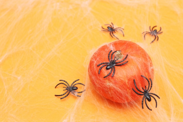 Calabaza de Halloween con telaraña y arañas negras sobre fondo naranja