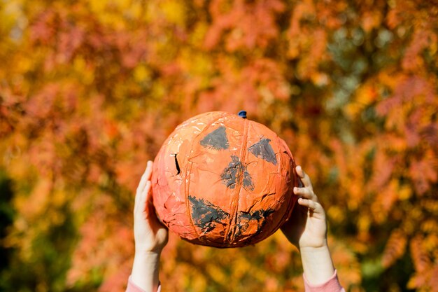 Calabaza hecha a mano en manos sobre fondo naranja otoñal. Concepto de Halloween, truco o trato.