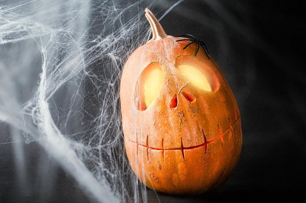 Calabaza JackoLantern resplandeciente y telarañas en la celebración de halloween de fondo oscuro