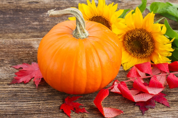 Una calabaza naranja con girasoles y hojas rojas de otoño sobre una mesa con textura de madera