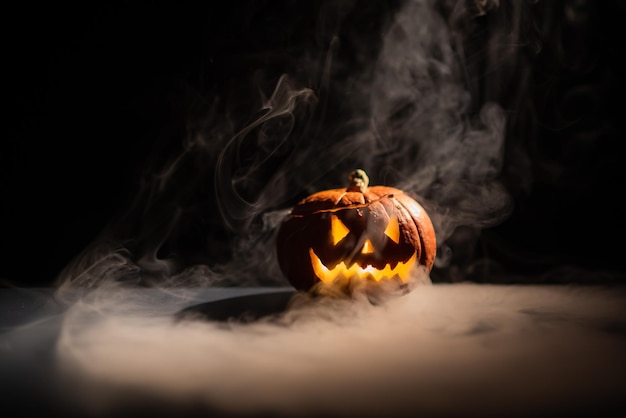 Calabaza naranja de Halloween con una cara luminosa aterradora sobre un fondo oscuro Un humo gris espeso sale y se esparce por la mesa negra Un primer plano de una linterna en la víspera de todos los santos