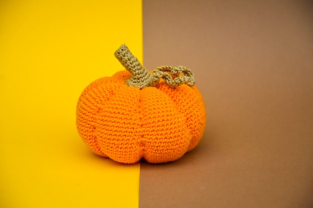 Una calabaza naranja tejida a ganchillo está aislada sobre un fondo amarillo beige Costura de otoño