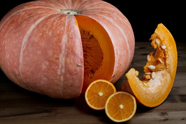 Calabaza orgánica entera fresca y mitades de naranjas en rodajas sobre un fondo de madera oscura