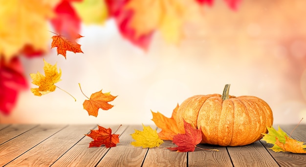 Calabaza y otoño hojas que caen sobre una mesa de madera con el telón de fondo de un parque de otoño