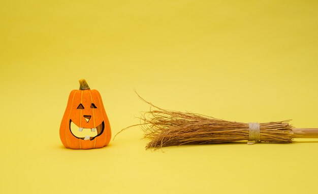 Calabaza pintada con una escoba sobre un fondo amarillo aislado