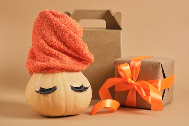 Calabaza con toalla y caja de regalo de pestañas postizas con cinta y despertador sobre fondo beige