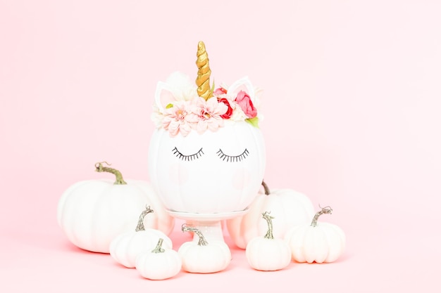 Calabaza unicornio blanca decorada con flores sobre un fondo rosa.