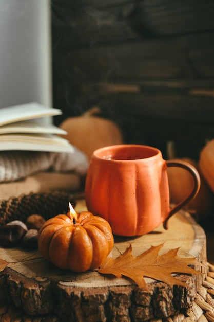 Calabaza de velas encendidas y una taza de té en el fondo de una pila de suéteres composición de otoño