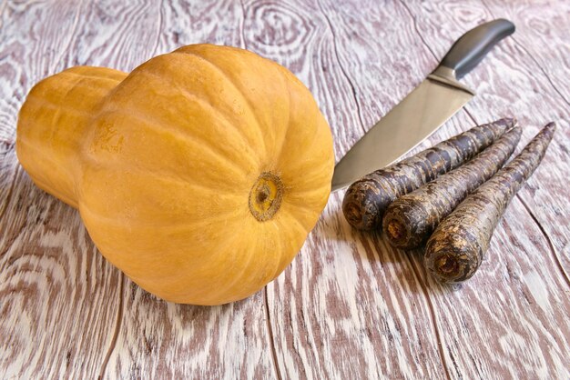 Calabaza, zanahoria negra cruda y cuchillo sobre una mesa de madera, poca profundidad de campo