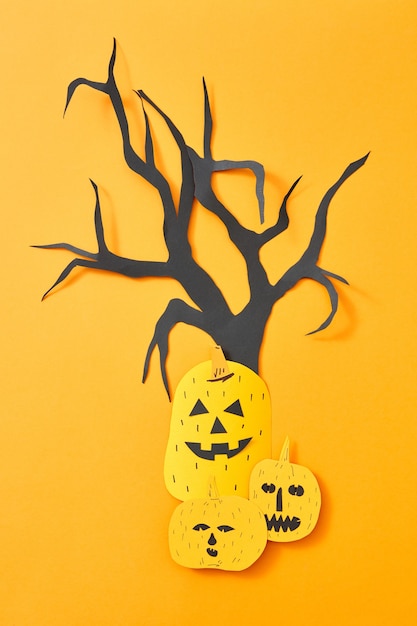 Calabazas aterradoras y un árbol de papel artesanal presentado sobre un fondo naranja con espacio de copia. Diseño creativo para Halloween. Endecha plana
