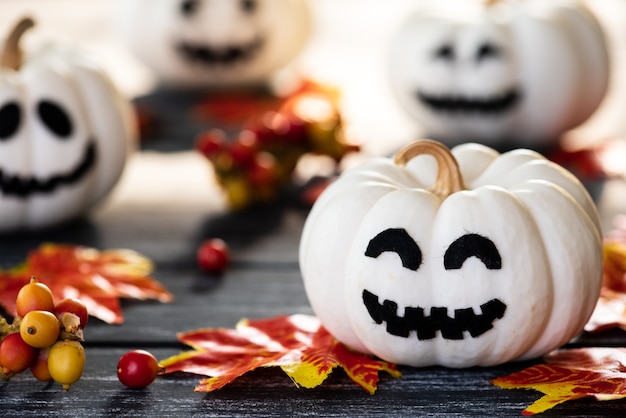 Calabazas blancas del fantasma con las hojas de otoño coloridas en un fondo de madera negro de la tabla.