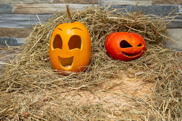 Calabazas de halloween rojas y amarillas se encuentran en el heno con el telón de fondo de una pared de piedra gris