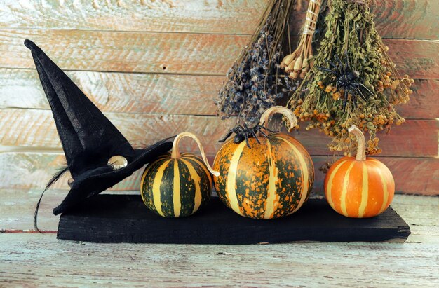 Calabazas de Halloween sombrero de bruja arañas y ramos de hierbas secas en una mesa de madera