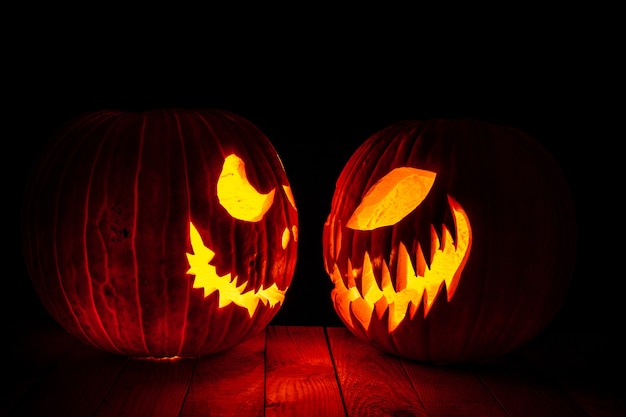 Calabazas de halloween talladas mirando el uno al otro, vista lateral. base de madera y fondo negro.