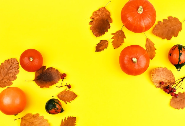 Calabazas naranjas con hojas de otoño sobre un fondo amarillo Concepto de cosecha Vista superior de Halloween Lugar para una inscripción