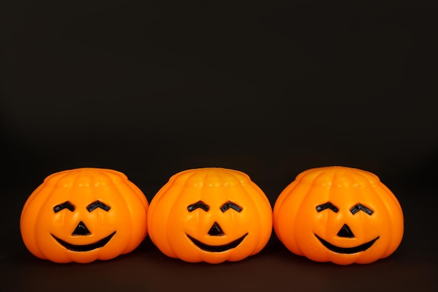 Las calabazas son de plástico naranja con caras sonrientes sobre un fondo negro. Postal con espacio de copia.