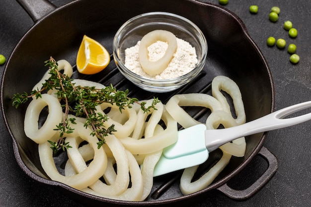 Calamares cortados en aros y ramitas de tomillo en una sartén Limón y harina en un bol Plano Fondo negro