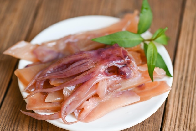 calamares encurtidos en un plato blanco, calamares crudos para cocinar alimentos en una mesa de madera, conservar los mariscos