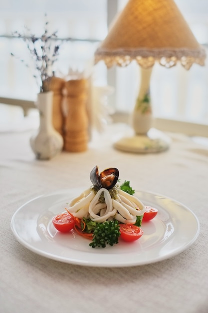 Calamares y mejillones con verduras en un plato blanco sobre un fondo blanco