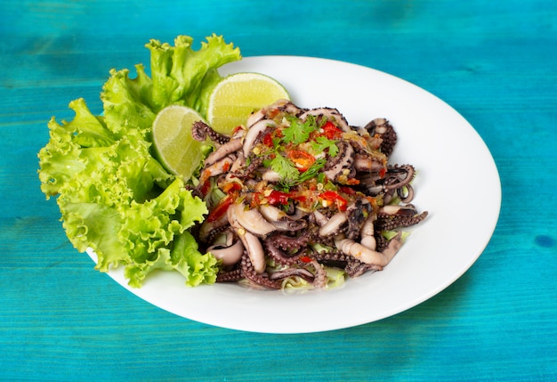 Calamares a la plancha con salsa de mariscos en un plato blanco con decoración de lechuga y limón colocados sobre una mesa de madera azul.