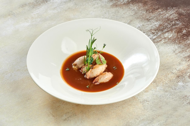 Calamares rellenos en salsa en un plato blanco sobre un mantel blanco