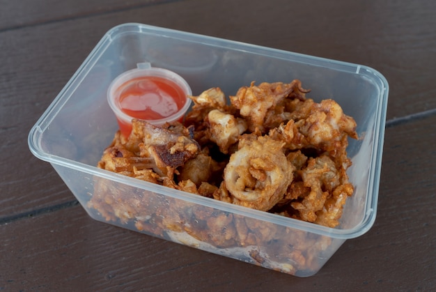 Calamares en rodajas fritas crujientes de primer plano con ajo servido en un recipiente para llevar con salsa de chile en la mesa de madera