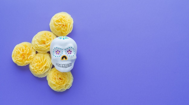 Calavera mexicana con flores amarillas de papel cempasuchil sobre violeta